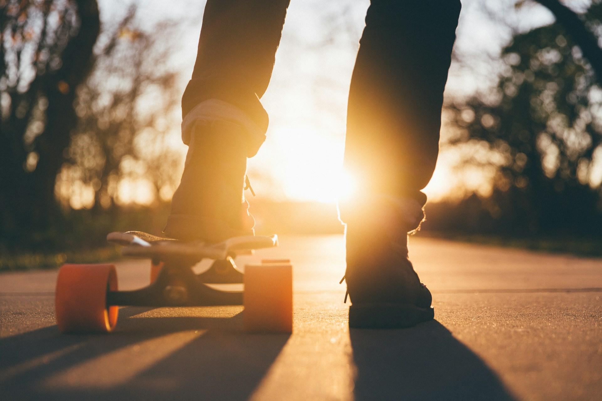 Man putting left foot on longboard against sunlight